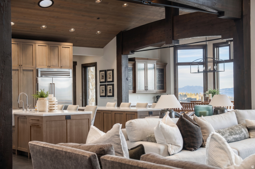 Open-concept interior featuring exposed wood beams, a kitchen island with seating, stainless steel refrigerator, recessed lighting, and large windows