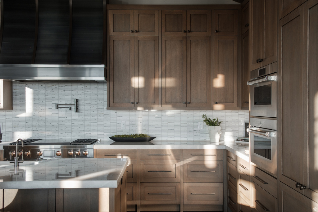 Gourmet kitchen featuring a professional-grade range, stainless steel appliances, custom wood cabinetry, stone countertops, and a full-height tile backsplash