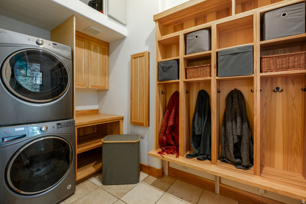 Integrated laundry area featuring wood-finish cabinetry, a stacked washer and dryer, and tile flooring
