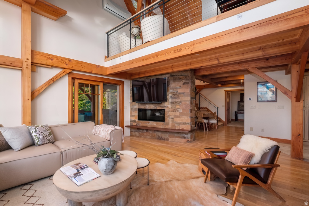 Spacious living area featuring exposed wood beams, a stone-clad fireplace with an integrated linear firebox, and light wood-finish flooring