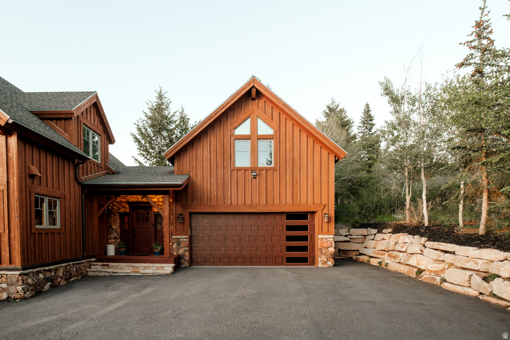 Wood-sided exterior featuring a modern garage door with frosted glass panels, an arched transom window, and a stone retaining wall