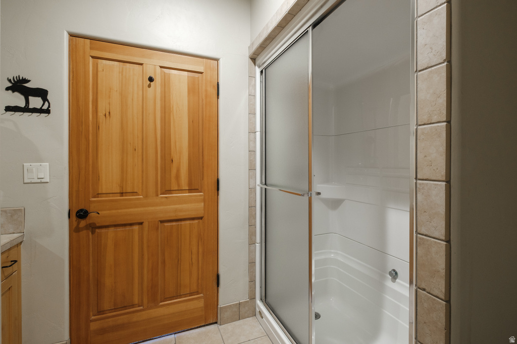 Four-panel wood door with black hardware, featuring a frosted glass shower enclosure with chrome accents, white shower surround, and neutral square tile detailing on the wall and flooring