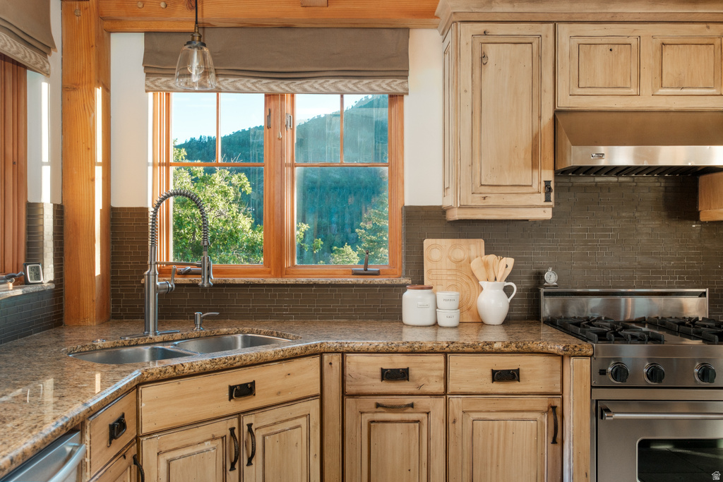 Kitchen featuring wood-frame windows, granite countertops, a double basin sink with a gooseneck faucet, a stainless steel range, and wood cabinetry with dark hardware