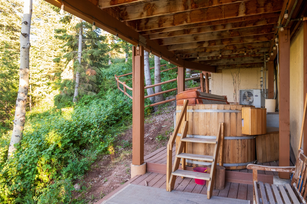 Expansive outdoor deck featuring a built-in wooden hot tub with stairs, string lighting, and an overhead wood-beam ceiling