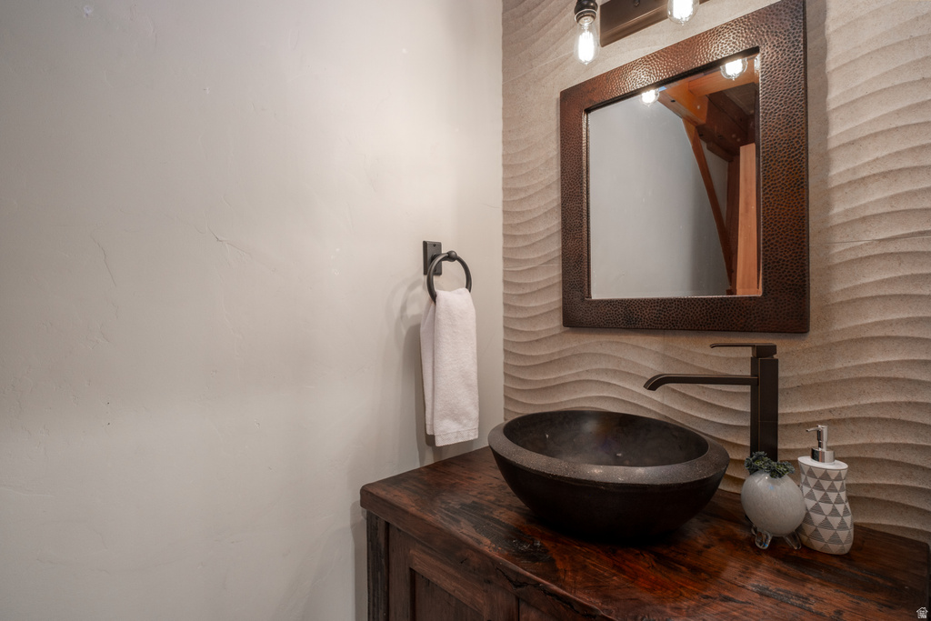 Powder room featuring a hammered copper framed mirror, wave-textured accent wall, dark wood vanity, vessel sink, and matte black faucet