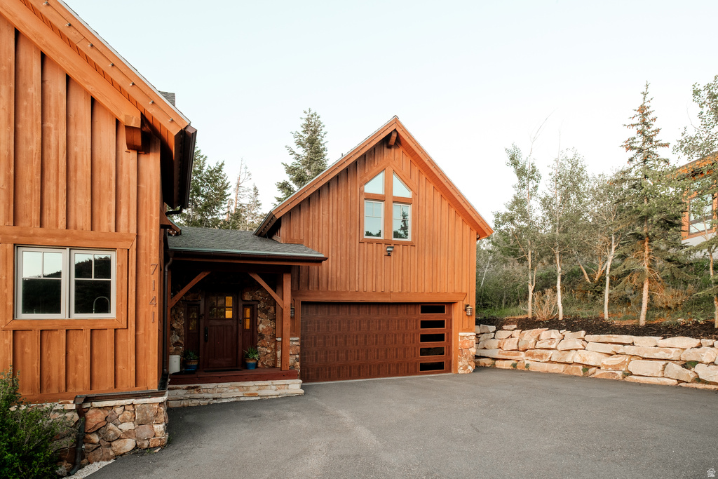Cabin-style exterior featuring board and batten siding with stone accents, a covered entry porch, an integrated two-car garage with contemporary glass panels, and a terraced rock retaining wall