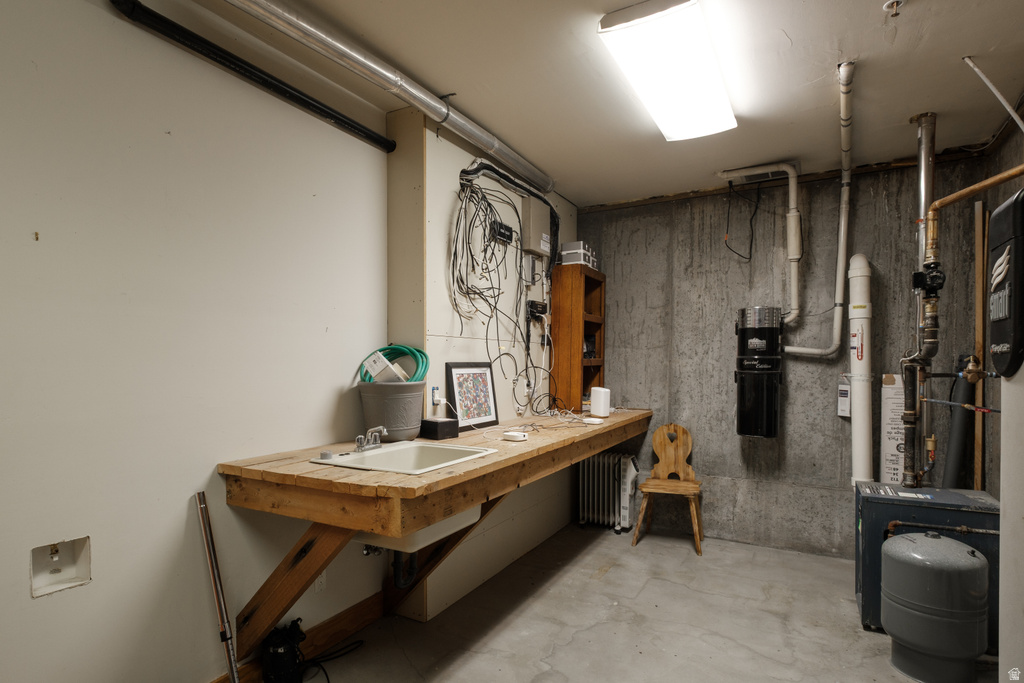 Utility area featuring a built-in workbench with an integrated sink and faucet, concrete flooring, and exposed concrete walls