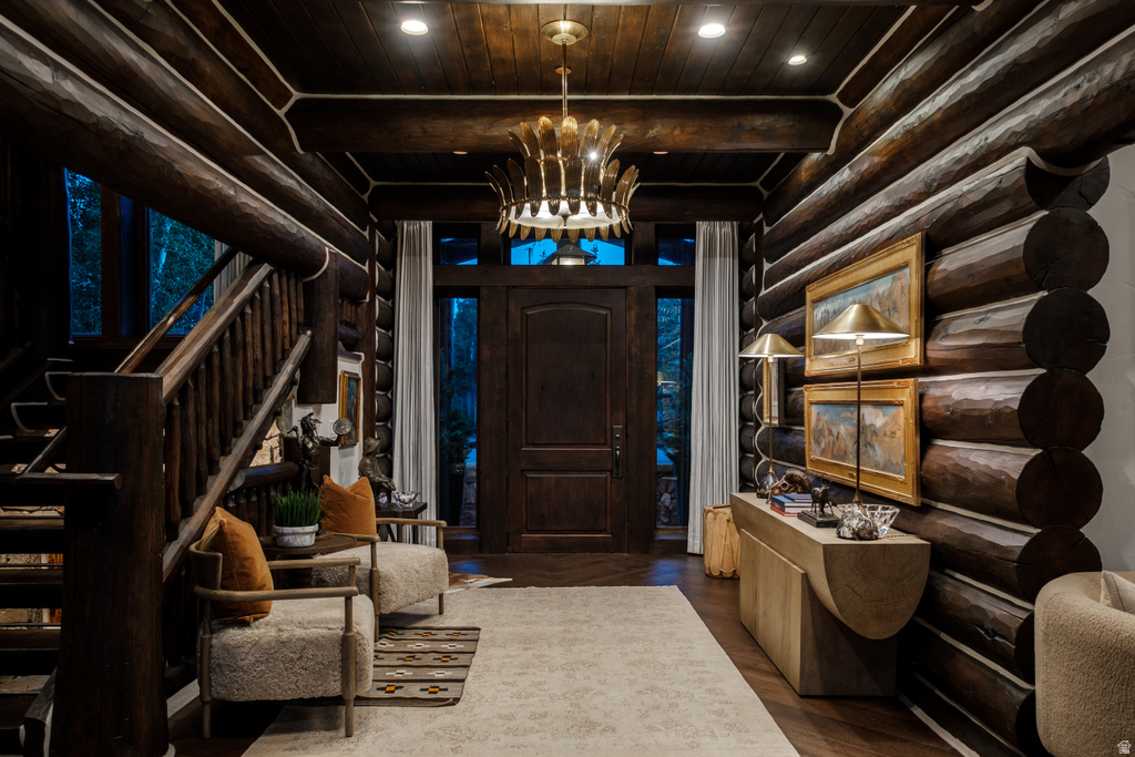 Grand entryway featuring log construction, a substantial wooden staircase, a decorative chandelier, and a solid wood entry door with sidelight windows