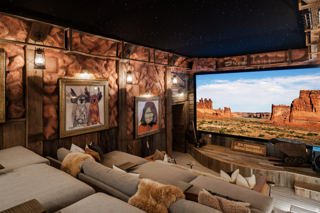 Dedicated home theater featuring a large projection screen, multi-level seating, a starry night ceiling, and rustic wood paneling with rock-like accents