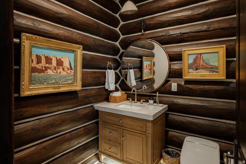 Powder room featuring log walls, a wood vanity with a white countertop, a circular mirror, and brass fixtures