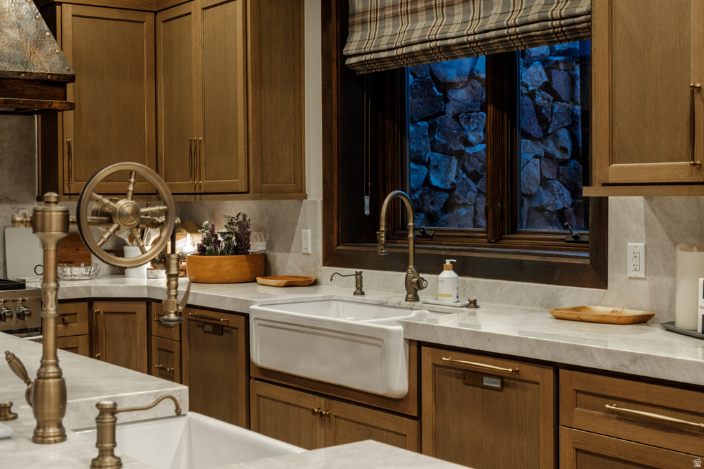 Gourmet kitchen featuring a farmhouse sink, wood-finish cabinetry, light-toned stone countertops, and bronze-finish fixtures