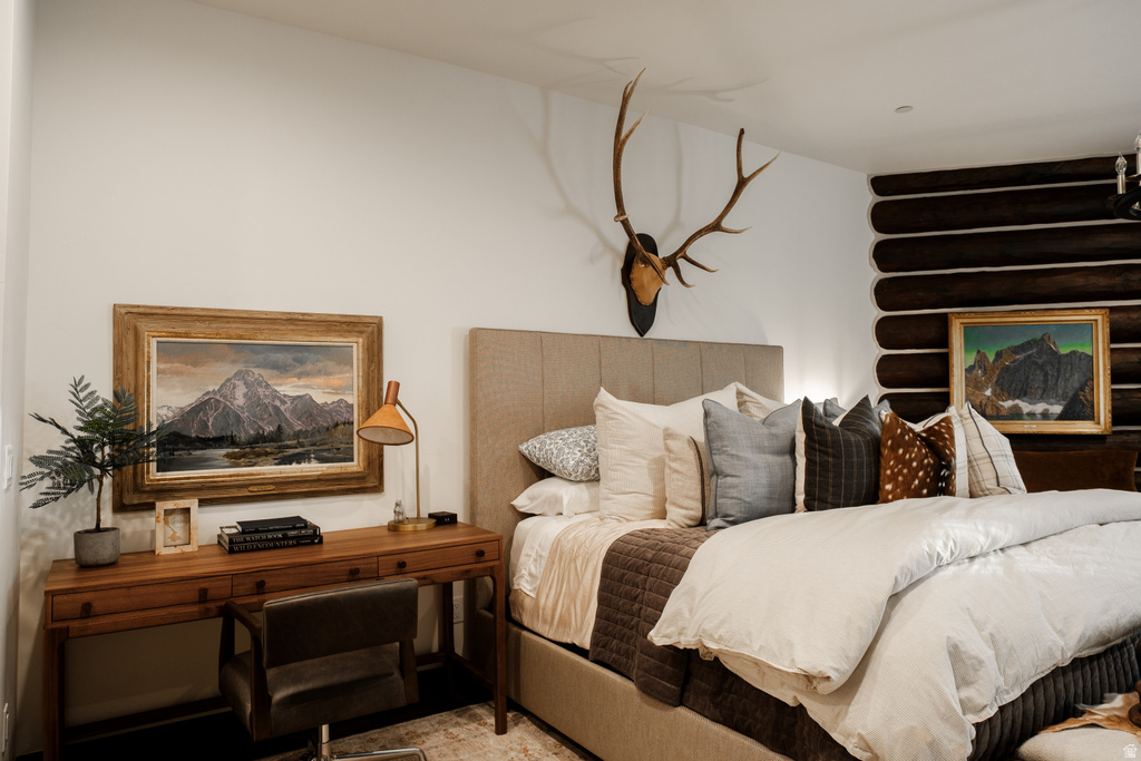 Bedroom featuring a beige upholstered headboard, a wood-finish desk, and a textured log wall detail