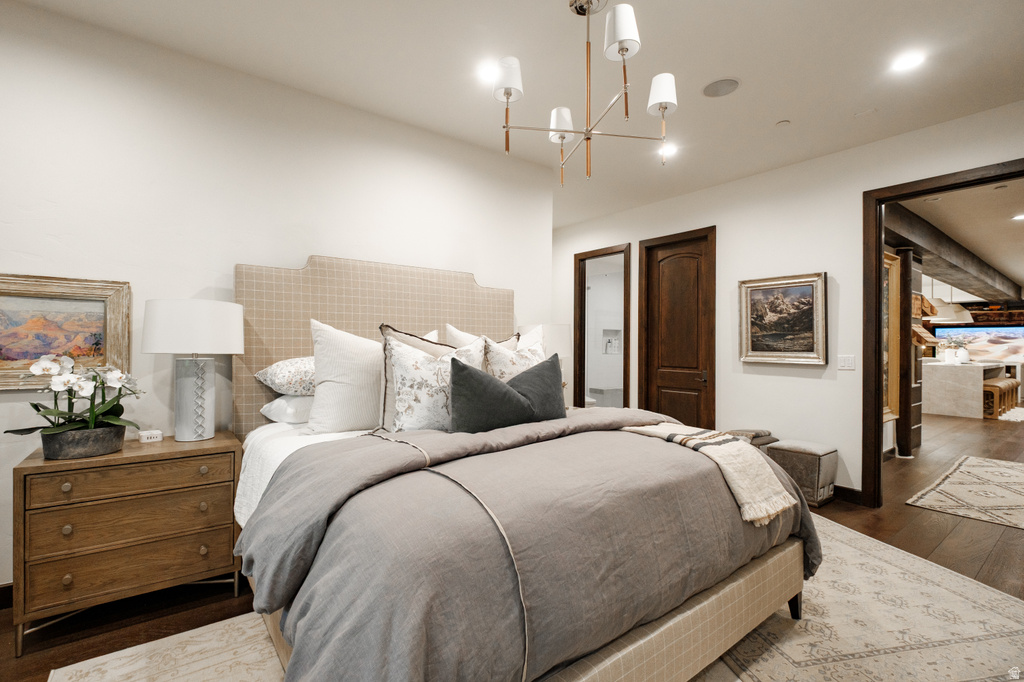 Bedroom featuring dark wood-finish flooring, a contemporary chandelier, recessed lighting, and a plaid upholstered headboard
