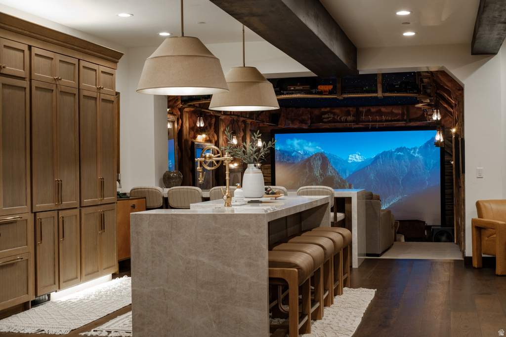 Open-concept living space featuring a large projection screen display, a stone-clad kitchen island with seating, integrated paneled appliances, and exposed ceiling beams