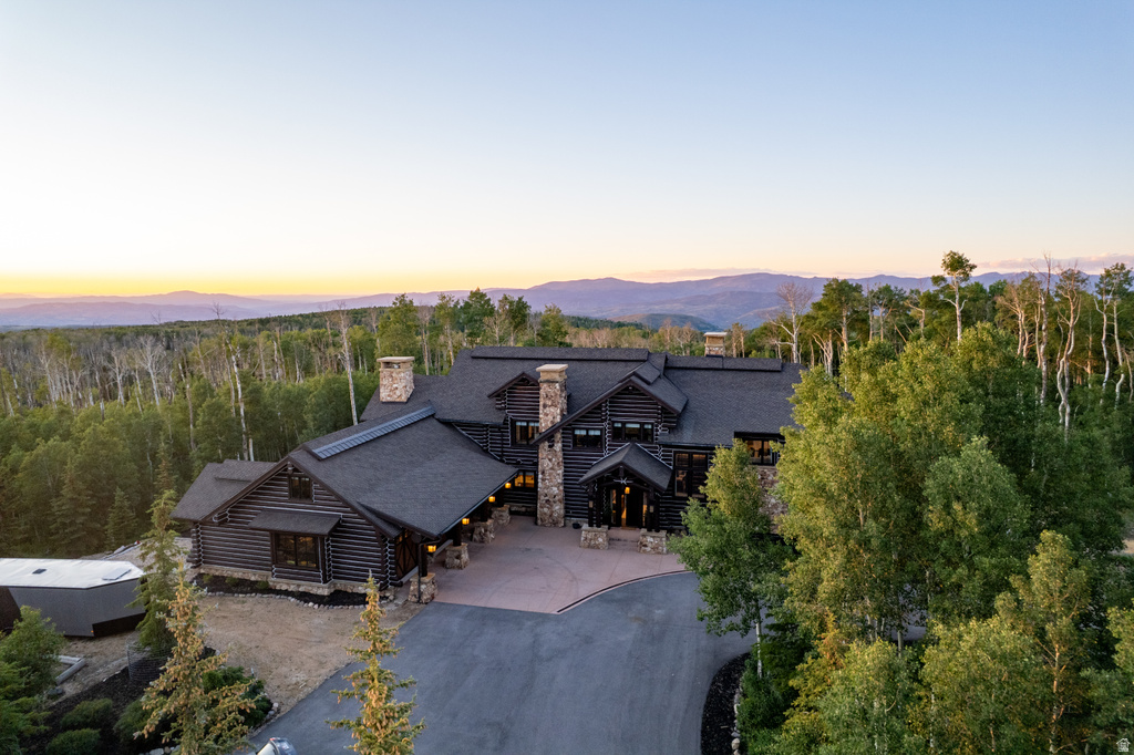Log home with multiple stone chimneys and a dark shingle roof