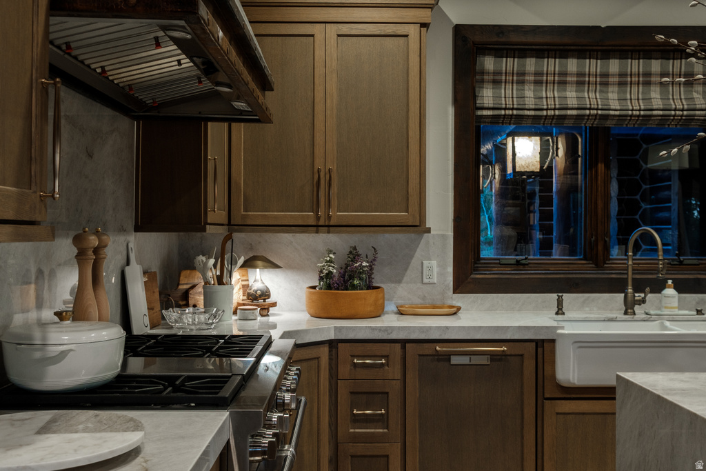 Kitchen featuring wood-finish cabinetry, light-toned countertops, a stainless steel range with overhead ventilation, and a white farmhouse sink