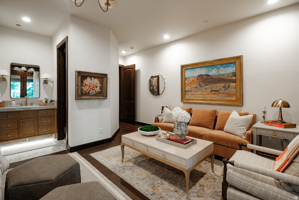 Wood-finish flooring with a decorative area rug, recessed lighting, and a chandelier illuminate this living space