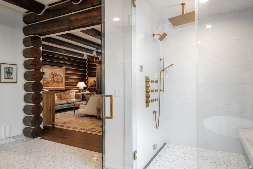 Spa-inspired shower with glass enclosure, white subway tile surround, ceiling-mounted gold-finish rainfall showerhead, and white pebble flooring