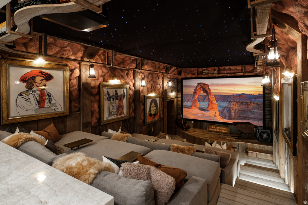 Theater room featuring a large projection screen, tiered seating, a starry night ceiling, textured rock walls, and wood-paneled accents