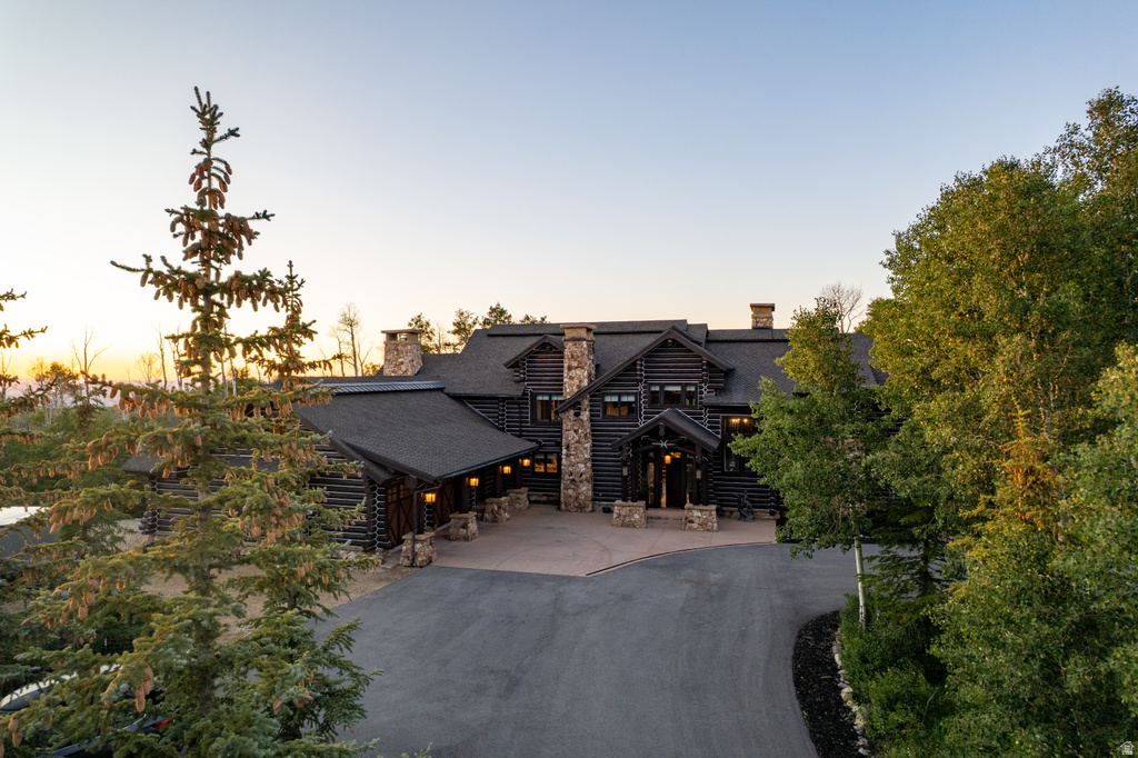 Expansive log home with multiple stone chimneys, a paved circular driveway, and a covered entry