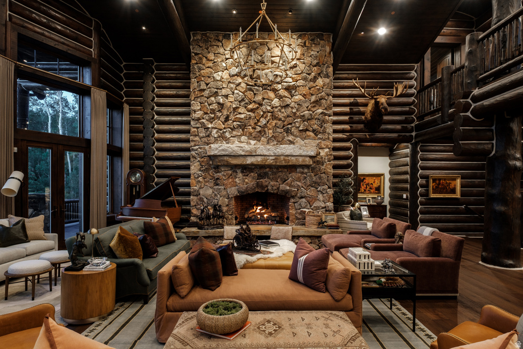 Great room featuring a floor-to-ceiling stone fireplace, exposed log walls, dark wood-finish flooring, a two-story window wall, and an upper-level balcony