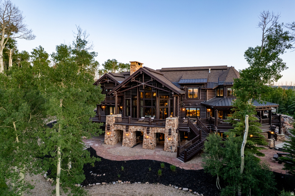 Multi-level log cabin exterior featuring a stone foundation, prominent stone chimney, multiple outdoor decks, and extensive window arrays