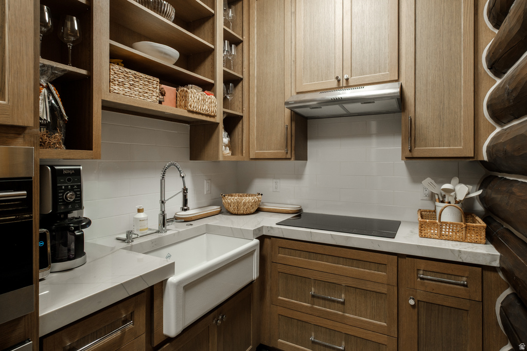 Kitchen featuring a white farmhouse sink with a gooseneck faucet, light-toned wood cabinetry, built-in cooktop, and a stainless steel range hood