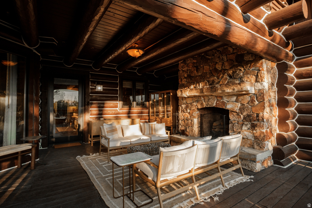 Covered outdoor living space featuring a stone fireplace, exposed log beams, wood-finish flooring, and a glass-paneled door