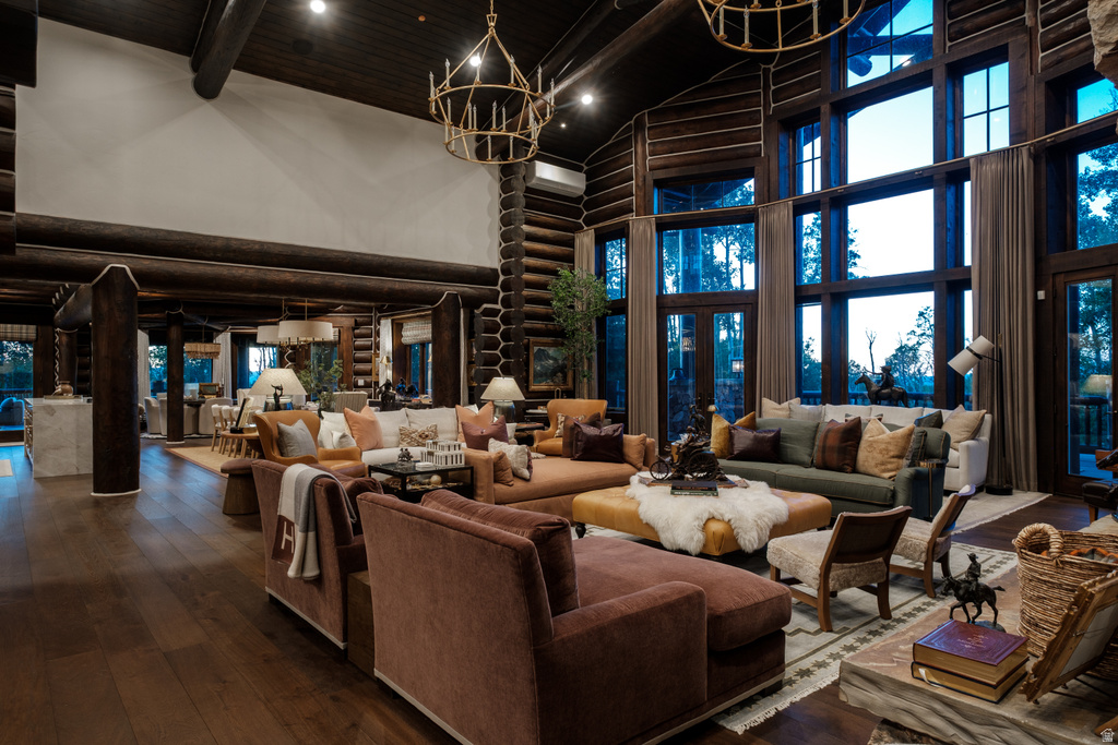 Expansive great room featuring a grand vaulted ceiling, floor-to-ceiling windows, exposed log beams, wood-finish flooring, and two brass chandeliers