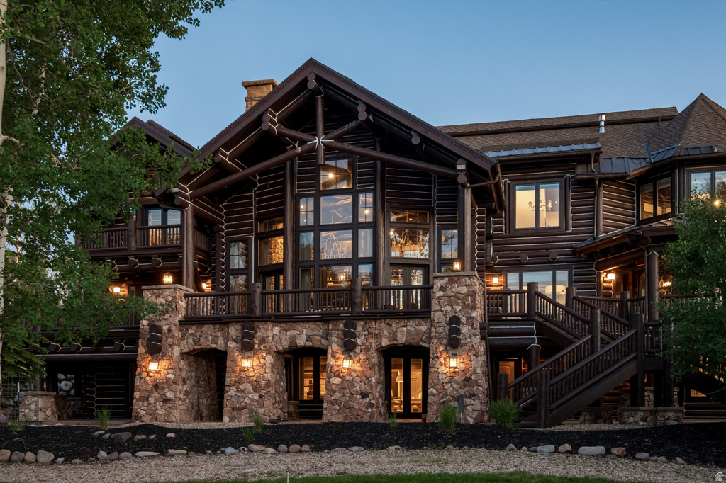 Expansive multi-level log home featuring a stone foundation, a two-story window wall, multiple balconies, a substantial exterior staircase, and exterior lighting fixtures