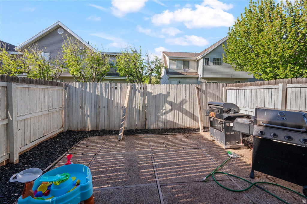 Paved patio area featuring a privacy fence, wood-chip landscaping, and a clear blue sky