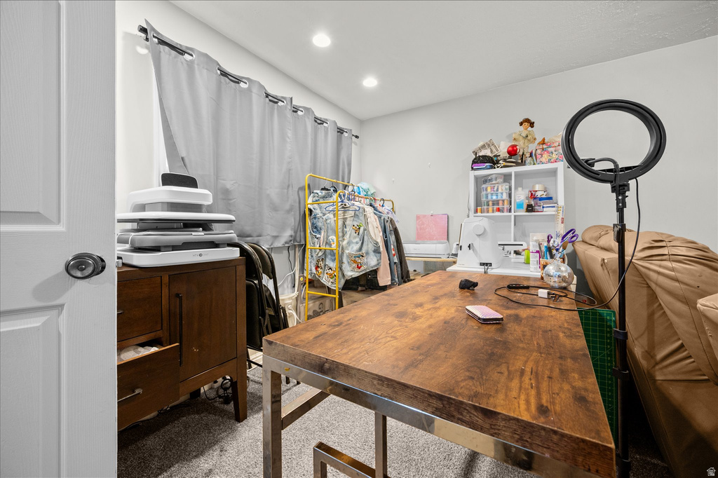 Recessed lighting illuminates a versatile room featuring light gray walls, plush carpet flooring, a window with gray drapes, and a white interior door