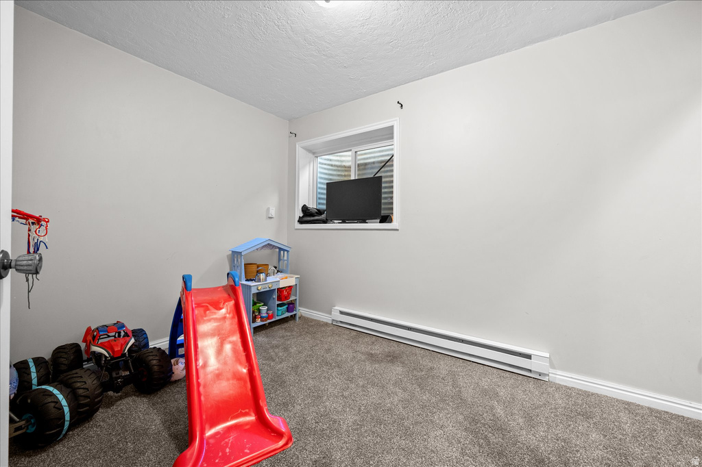 Interior room featuring neutral wall paint, grey carpet, a single window with blinds, and a baseboard heater