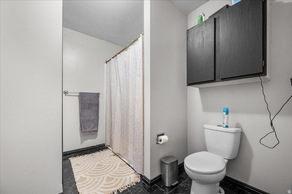 Bathroom featuring black tile flooring, white walls, and a white toilet