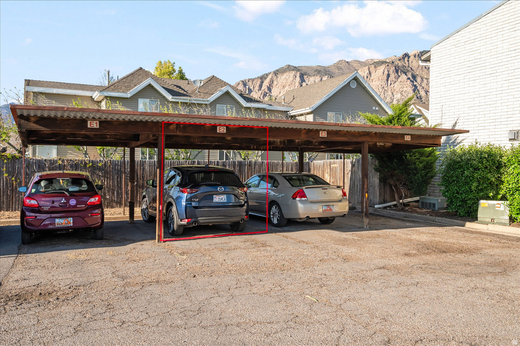 Covered parking space with marked designation, featuring a corrugated metal roof, wood support beams, and a gravel parking surface