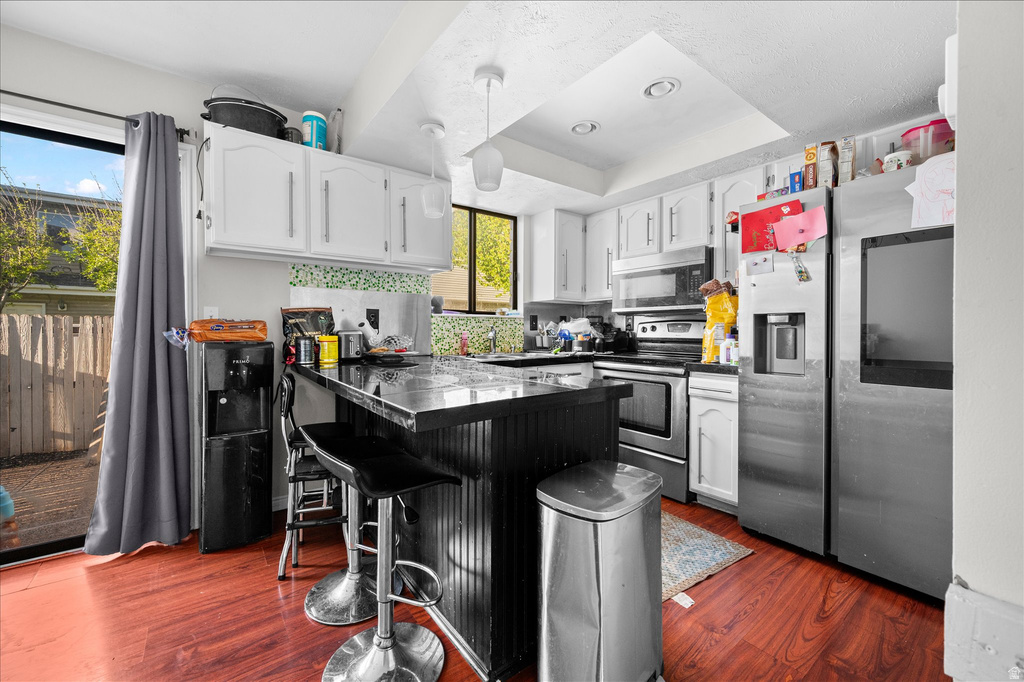 Kitchen featuring wood-finish flooring, white cabinetry, a central island with a dark countertop, stainless steel appliances, and a sliding glass door