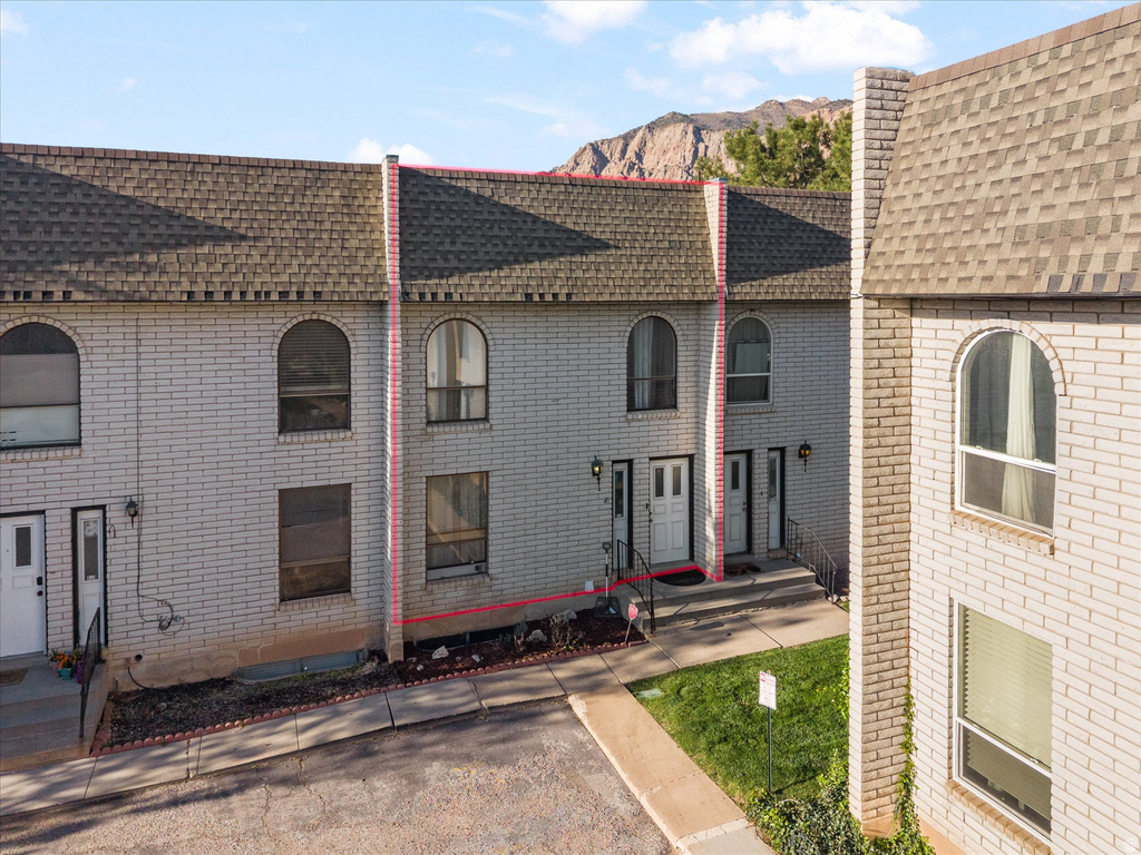 Townhome exterior featuring light-colored brick facade, arched upper windows, a multi-pane front door, exterior lighting fixtures, and a shingled roof