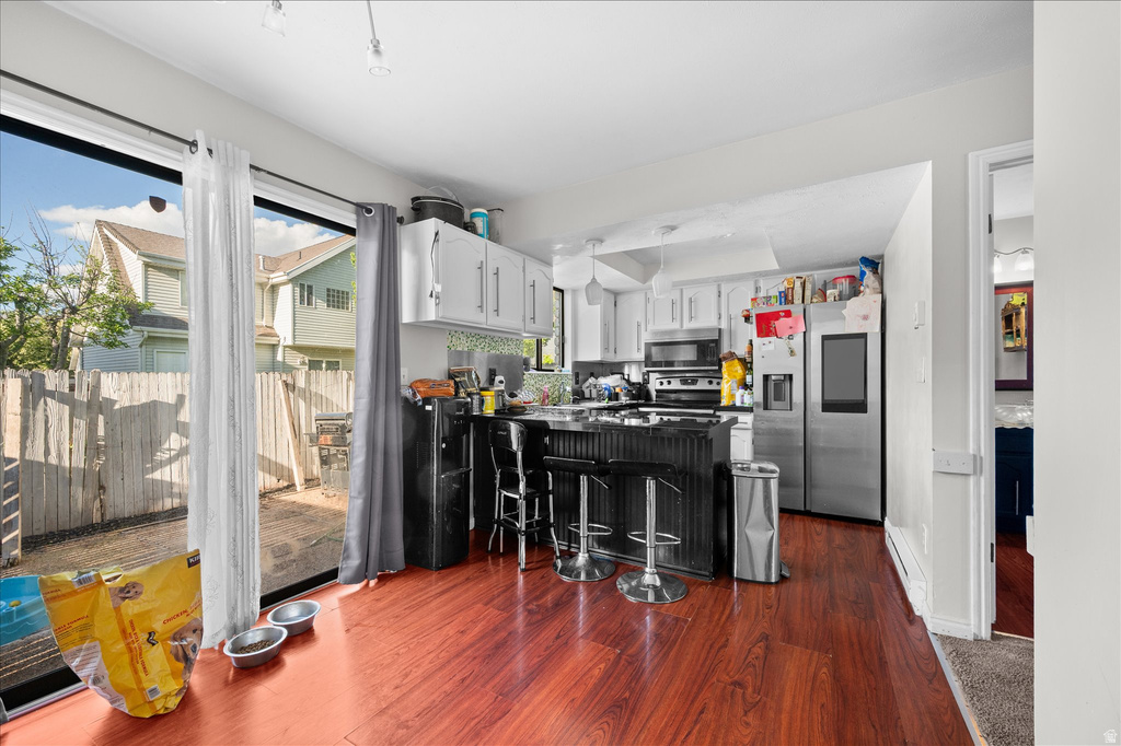 Kitchen featuring wood-finish flooring, white upper cabinetry, stainless steel appliances, and a breakfast bar with seating