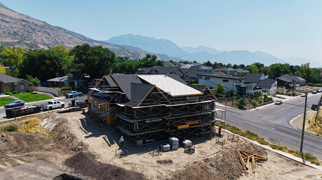Multi-level structure under construction with dark shingle roofing and mountain backdrop