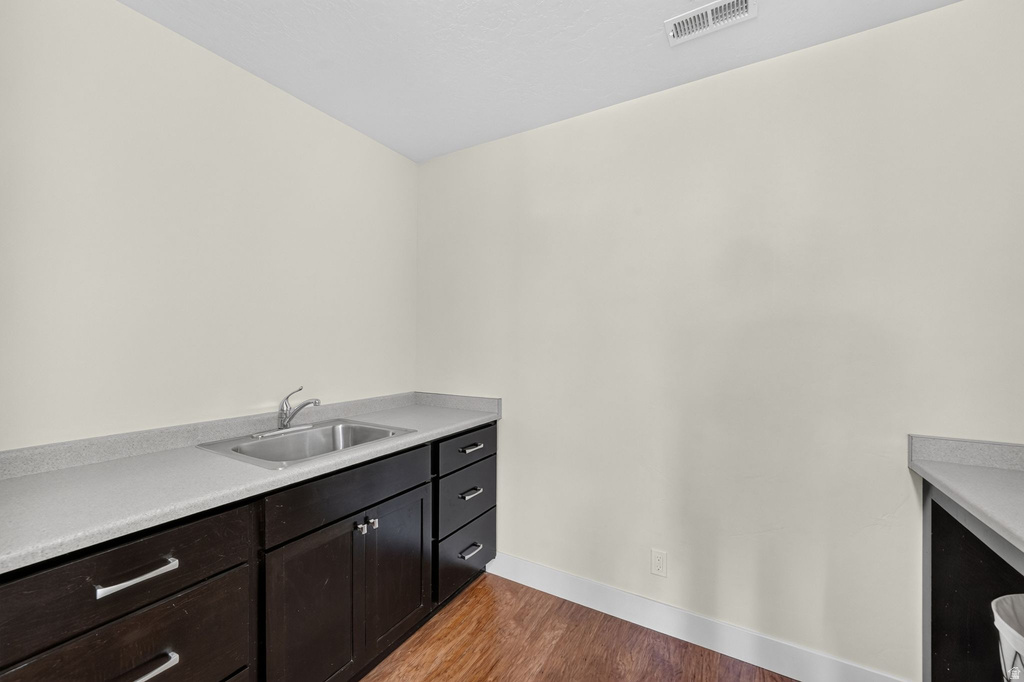 Service area featuring a stainless steel sink, dark wood-finish cabinetry, light grey countertops, and wood-finish flooring