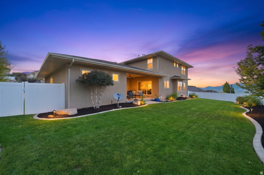 Expansive rear yard featuring a manicured lawn and defined landscaping beds with accent lighting