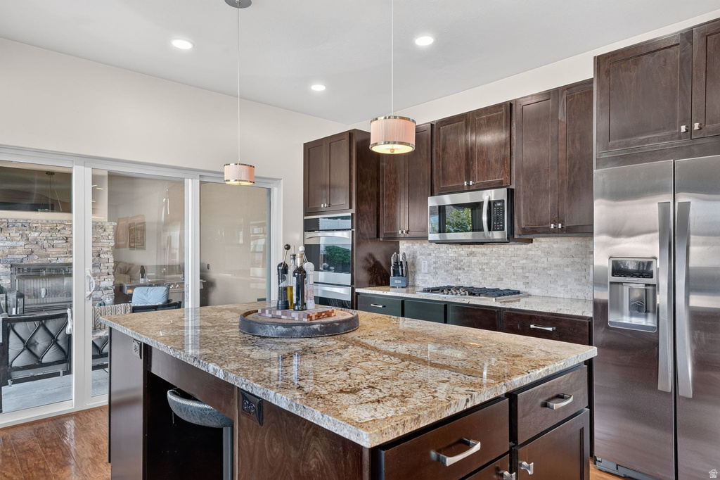 Kitchen featuring a large island with a stone countertop, dark wood cabinetry, stainless steel appliances, and a tile backsplash
