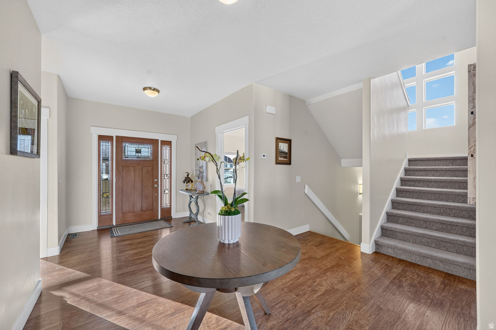 Spacious entryway featuring rich wood-finish flooring, a wood entry door with decorative glass sidelights, and a staircase with neutral carpeting