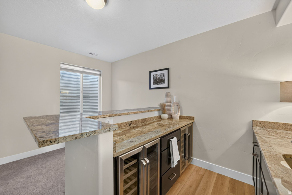Wet bar featuring granite countertops, undermount sink, beverage refrigerator, wine cooler, and light wood-finish flooring