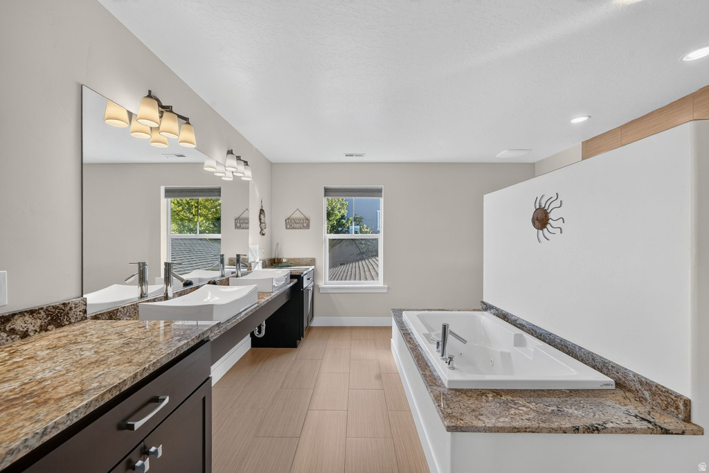 Expansive bathroom featuring a built-in soaking tub with a stone-finish surround, dual vanity with vessel sinks and stone-finish countertops, and wood-finish flooring