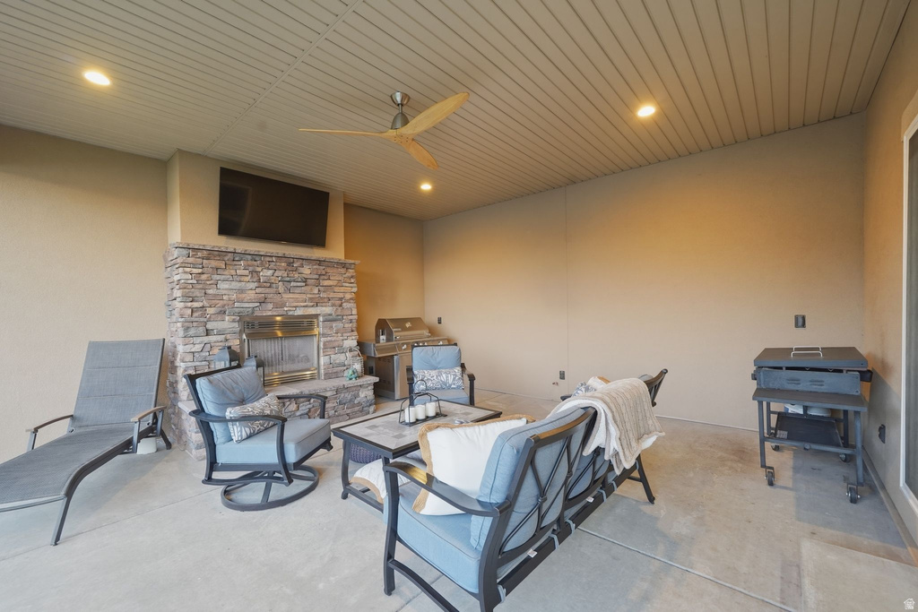 Covered patio featuring a stone-clad fireplace, integrated television, and a wood-bladed ceiling fan