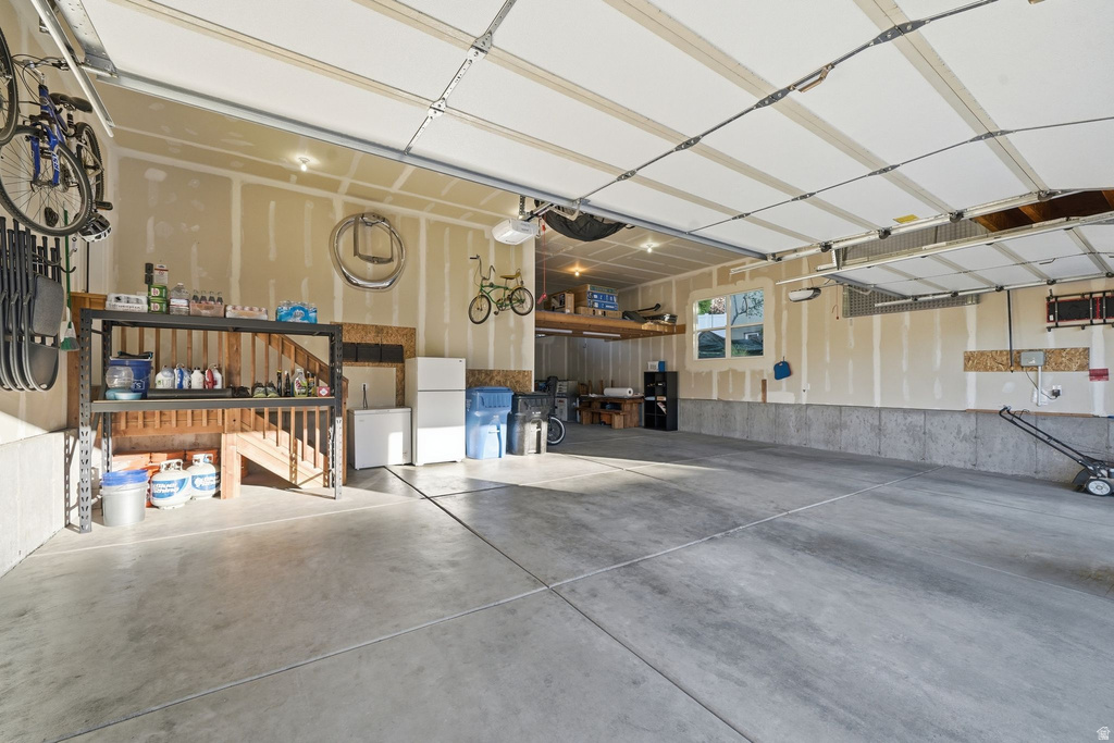Spacious garage with multiple garage doors, concrete flooring, built-in shelving, a finished ceiling, and an upper storage shelf