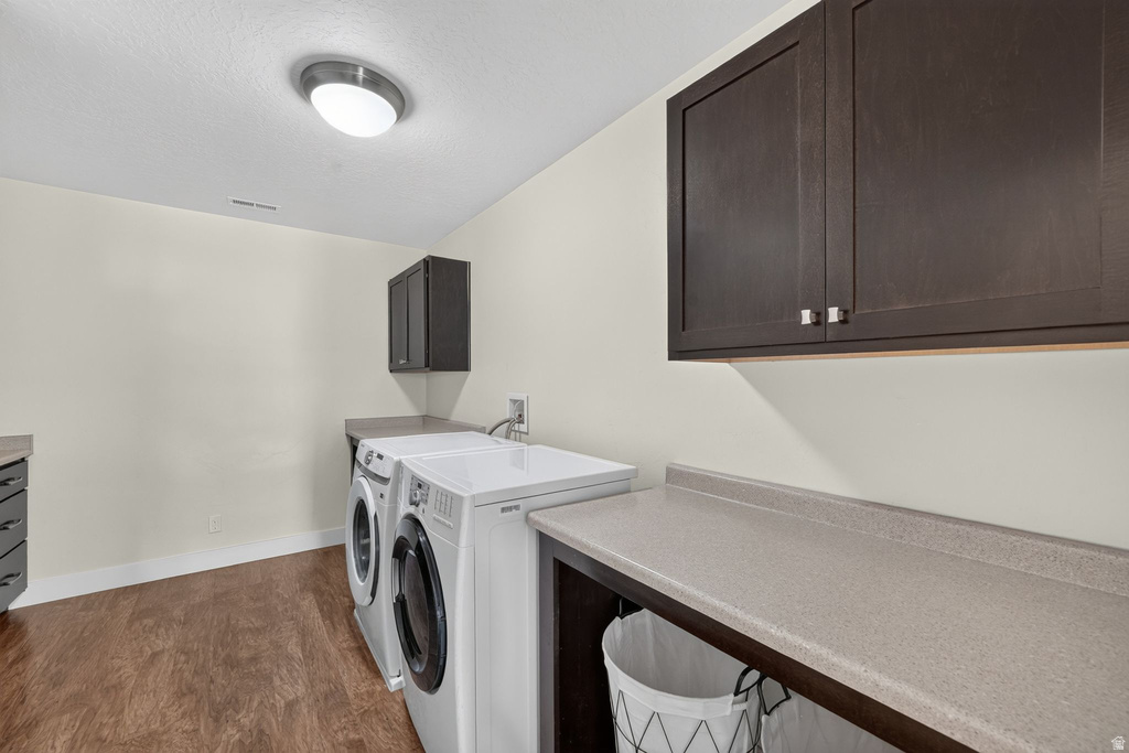 Laundry area featuring wood-finish flooring, light-colored walls, dark wood cabinetry, and a light-toned countertop