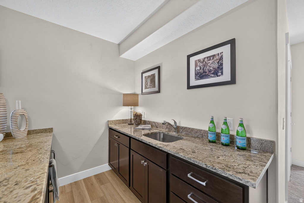 Compact wet bar featuring granite countertops, a stainless steel sink, dark wood-finish cabinetry, and wood-finish flooring