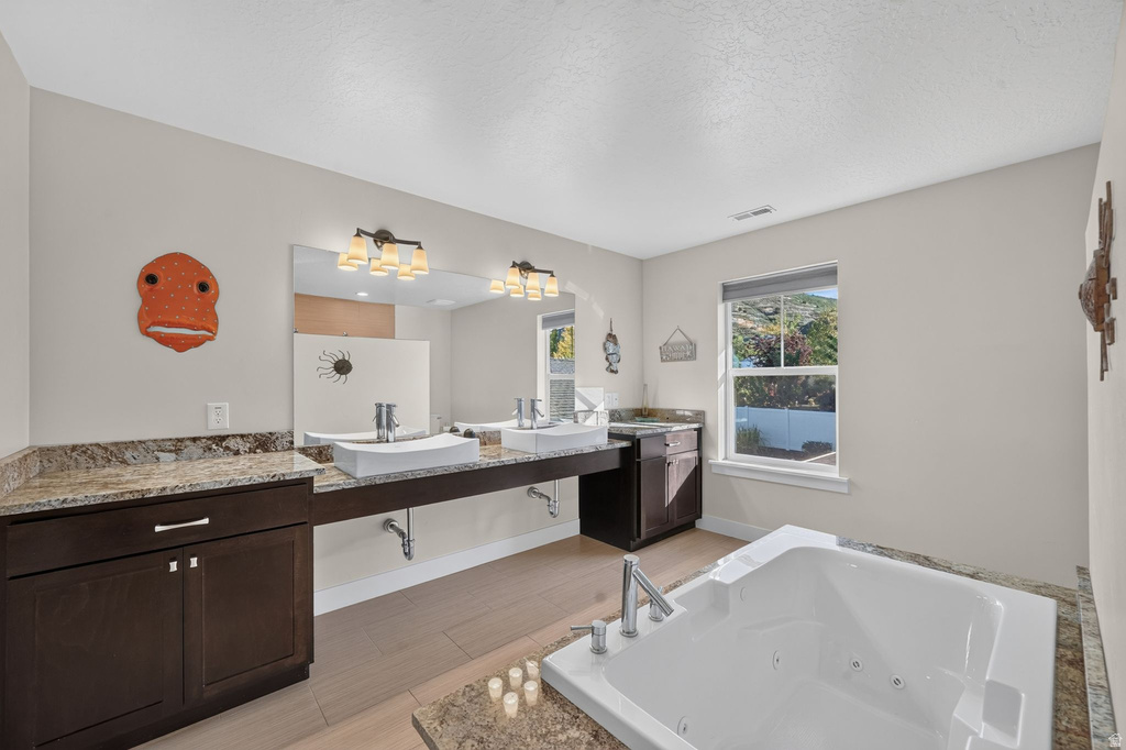 Bathroom featuring a built-in jetted tub, dual vanity with vessel sinks, dark wood cabinetry, and granite countertops